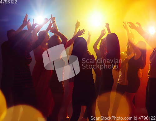 Image of A crowd of people in silhouette raises their hands against colorful neon light on party background