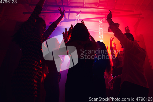 Image of A crowd of people in silhouette raises their hands against colorful neon light on party background