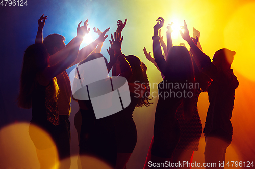 Image of A crowd of people in silhouette raises their hands against colorful neon light on party background
