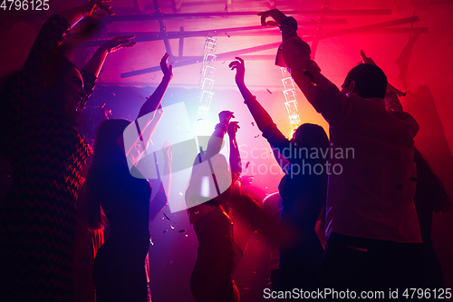 Image of A crowd of people in silhouette raises their hands against colorful neon light on party background