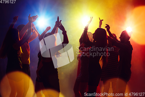 Image of A crowd of people in silhouette raises their hands against colorful neon light on party background