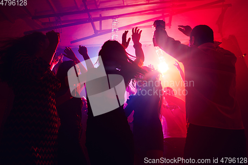 Image of A crowd of people in silhouette raises their hands against colorful neon light on party background