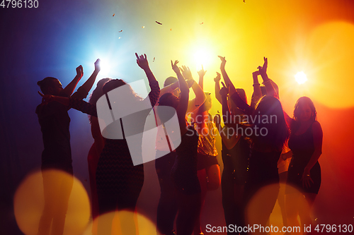 Image of A crowd of people in silhouette raises their hands against colorful neon light on party background