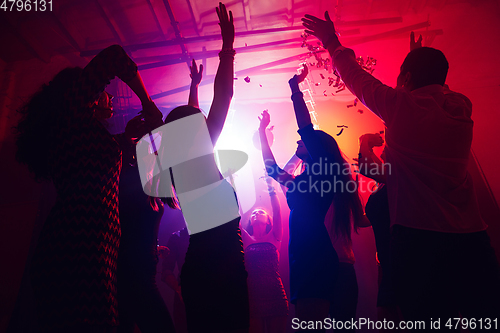 Image of A crowd of people in silhouette raises their hands against colorful neon light on party background