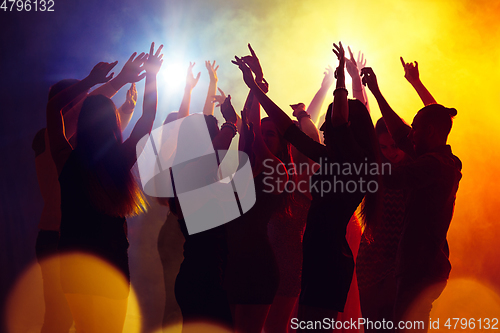 Image of A crowd of people in silhouette raises their hands against colorful neon light on party background