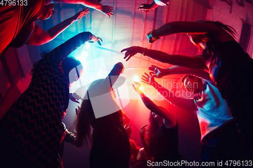 Image of A crowd of people in silhouette raises their hands against colorful neon light on party background