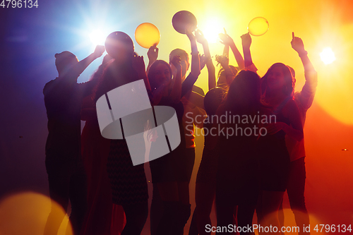 Image of A crowd of people in silhouette raises their hands against colorful neon light on party background