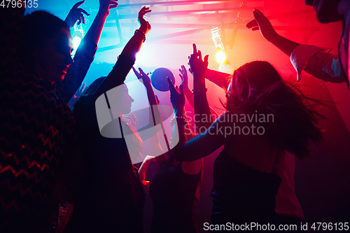 Image of A crowd of people in silhouette raises their hands against colorful neon light on party background