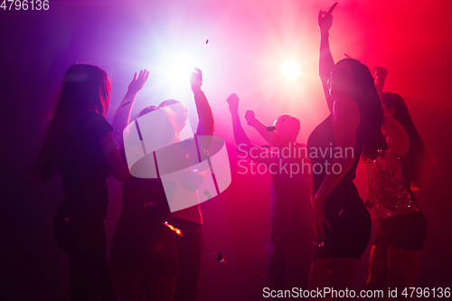 Image of A crowd of people in silhouette raises their hands against colorful neon light on party background