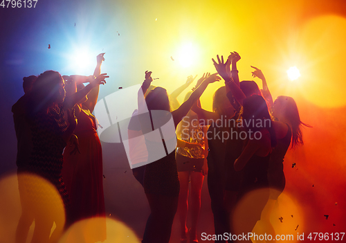 Image of A crowd of people in silhouette raises their hands against colorful neon light on party background