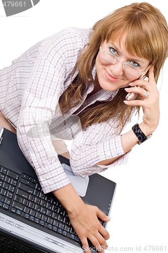 Image of The smiling young woman sits with the laptop and phone. Isolated