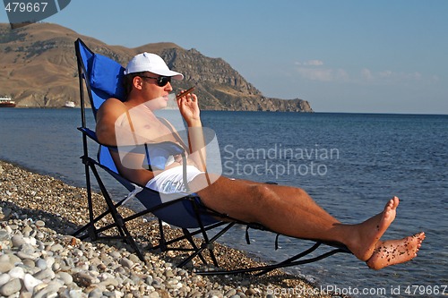 Image of The young man in sunglasses with a cigar has a rest on seacoast