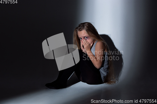 Image of Sad and frightened little girl with bloodshot and bruised eyes sitting scared