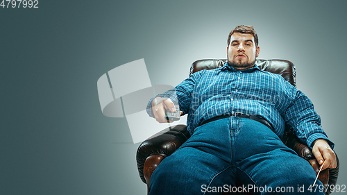 Image of Fat man sitting in a brown armchair, emotional watching TV