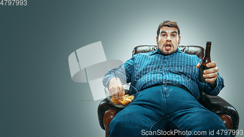 Image of Fat man sitting in a brown armchair, emotional watching TV