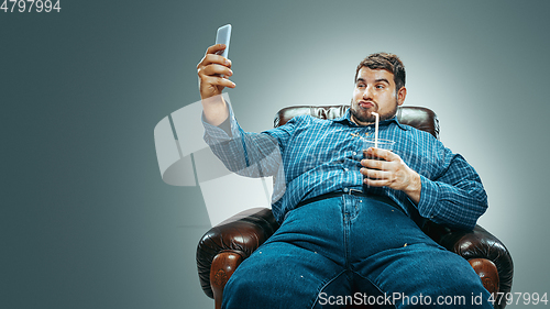 Image of Fat man sitting in a brown armchair, emotional watching TV