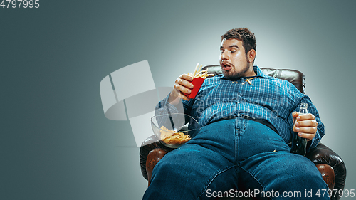 Image of Fat man sitting in a brown armchair, emotional watching TV