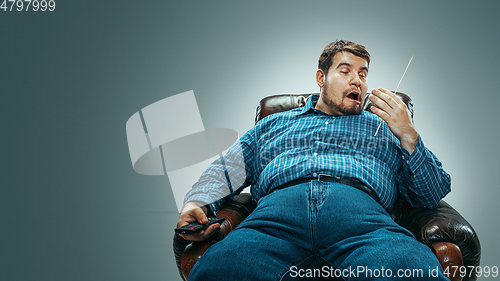 Image of Fat man sitting in a brown armchair, emotional watching TV