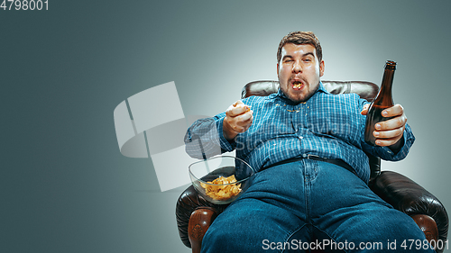 Image of Fat man sitting in a brown armchair, emotional watching TV