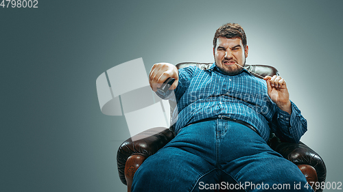 Image of Fat man sitting in a brown armchair, emotional watching TV