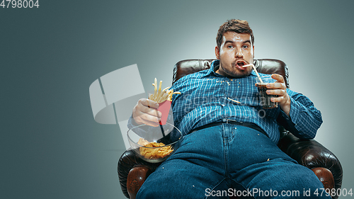 Image of Fat man sitting in a brown armchair, emotional watching TV