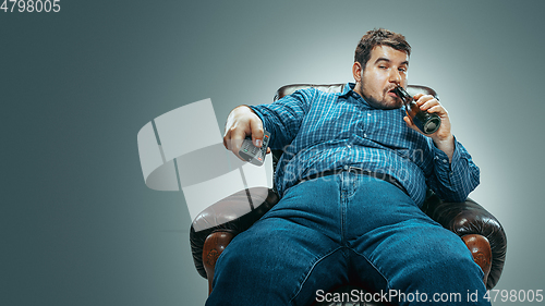 Image of Fat man sitting in a brown armchair, emotional watching TV