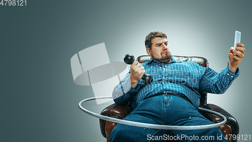 Image of Fat man sitting in a brown armchair, emotional watching TV