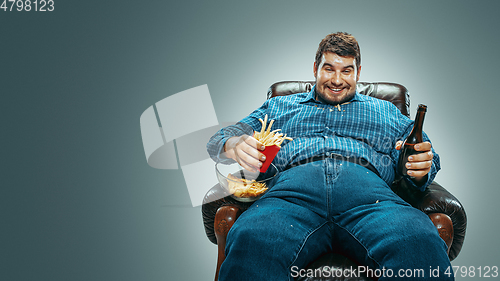 Image of Fat man sitting in a brown armchair, emotional watching TV