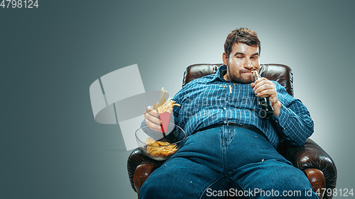 Image of Fat man sitting in a brown armchair, emotional watching TV