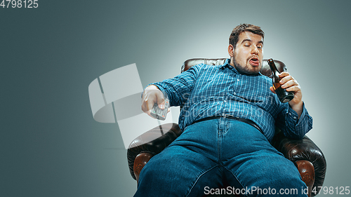 Image of Fat man sitting in a brown armchair, emotional watching TV