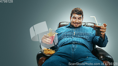 Image of Fat man sitting in a brown armchair, emotional watching TV