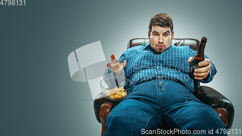 Image of Fat man sitting in a brown armchair, emotional watching TV