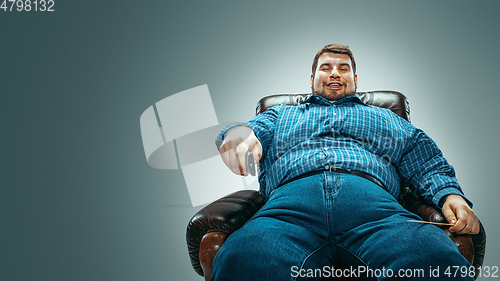 Image of Fat man sitting in a brown armchair, emotional watching TV