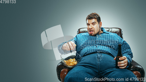 Image of Fat man sitting in a brown armchair, emotional watching TV