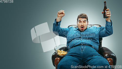 Image of Fat man sitting in a brown armchair, emotional watching TV