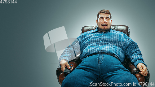 Image of Fat man sitting in a brown armchair, emotional watching TV