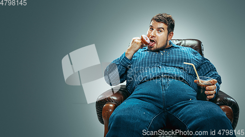 Image of Fat man sitting in a brown armchair, emotional watching TV