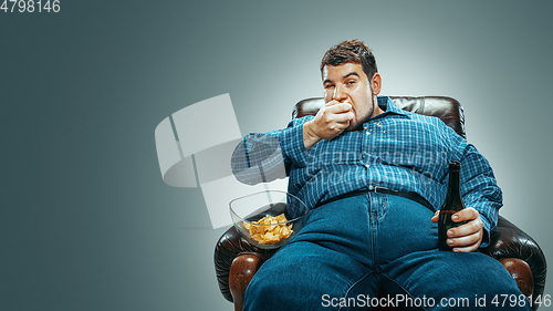 Image of Fat man sitting in a brown armchair, emotional watching TV