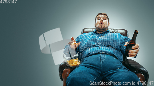 Image of Fat man sitting in a brown armchair, emotional watching TV