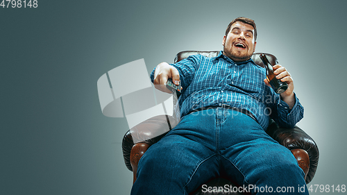 Image of Fat man sitting in a brown armchair, emotional watching TV