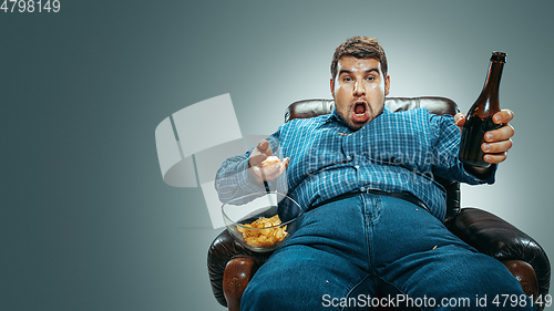 Image of Fat man sitting in a brown armchair, emotional watching TV