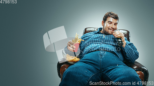 Image of Fat man sitting in a brown armchair, emotional watching TV