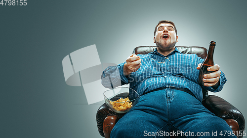 Image of Fat man sitting in a brown armchair, emotional watching TV