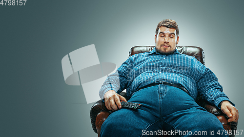 Image of Fat man sitting in a brown armchair, emotional watching TV