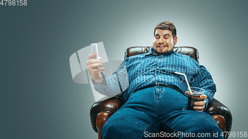 Image of Fat man sitting in a brown armchair, emotional watching TV