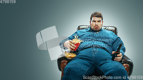 Image of Fat man sitting in a brown armchair, emotional watching TV