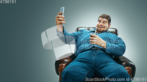 Image of Fat man sitting in a brown armchair, emotional watching TV