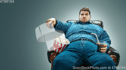 Image of Fat man sitting in a brown armchair, emotional watching TV