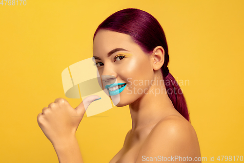 Image of Portrait of beautiful young woman with bright make-up isolated on yellow studio background