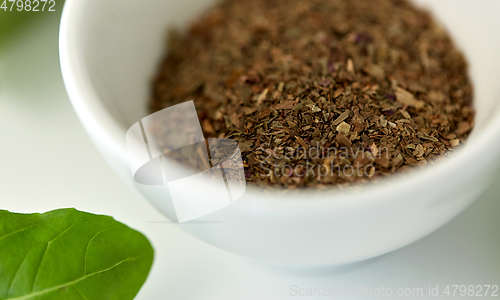 Image of close up of dry basil seasoning in white cup